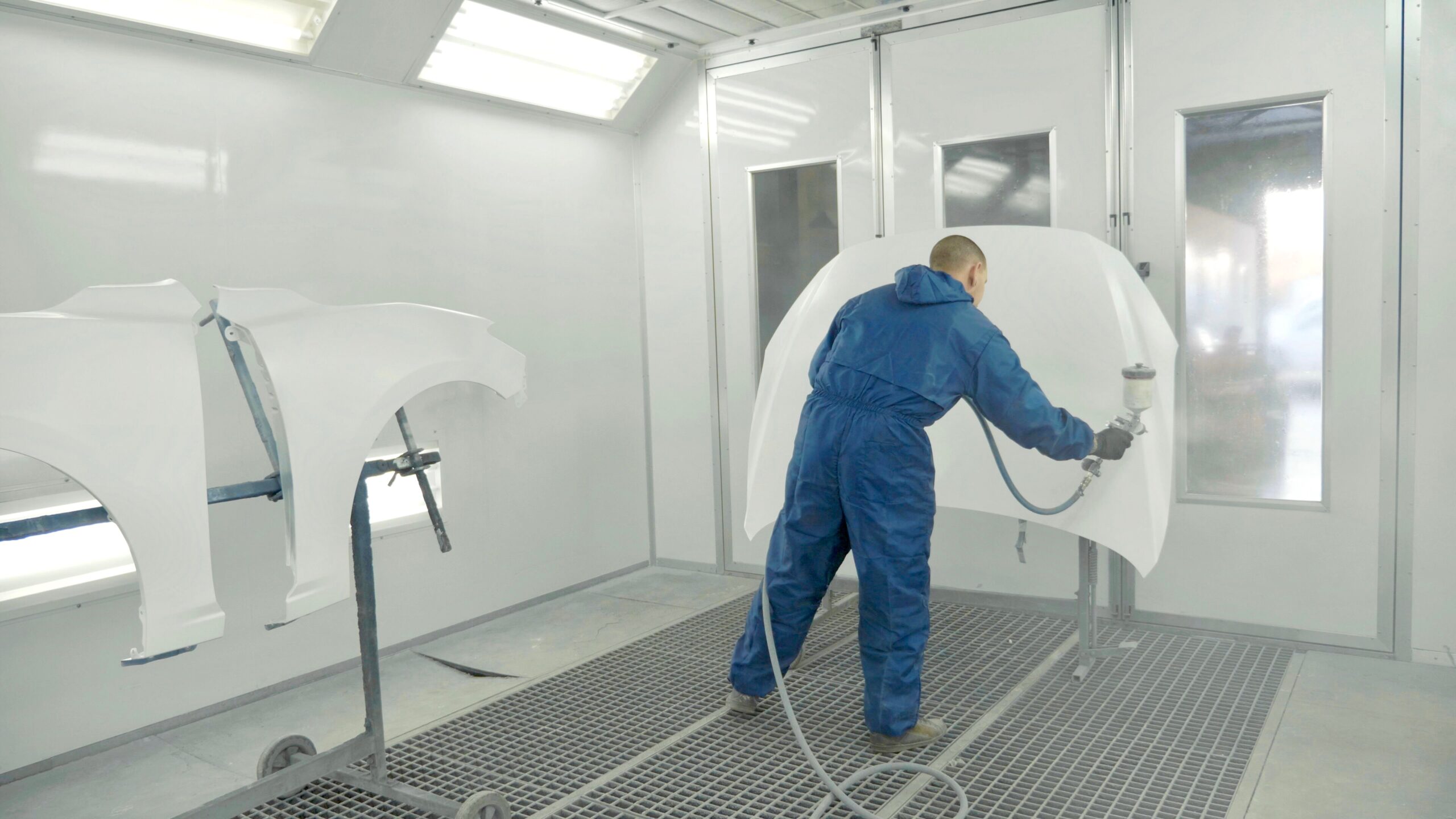 Home auto painter spraying white paint on car hood in special booth
